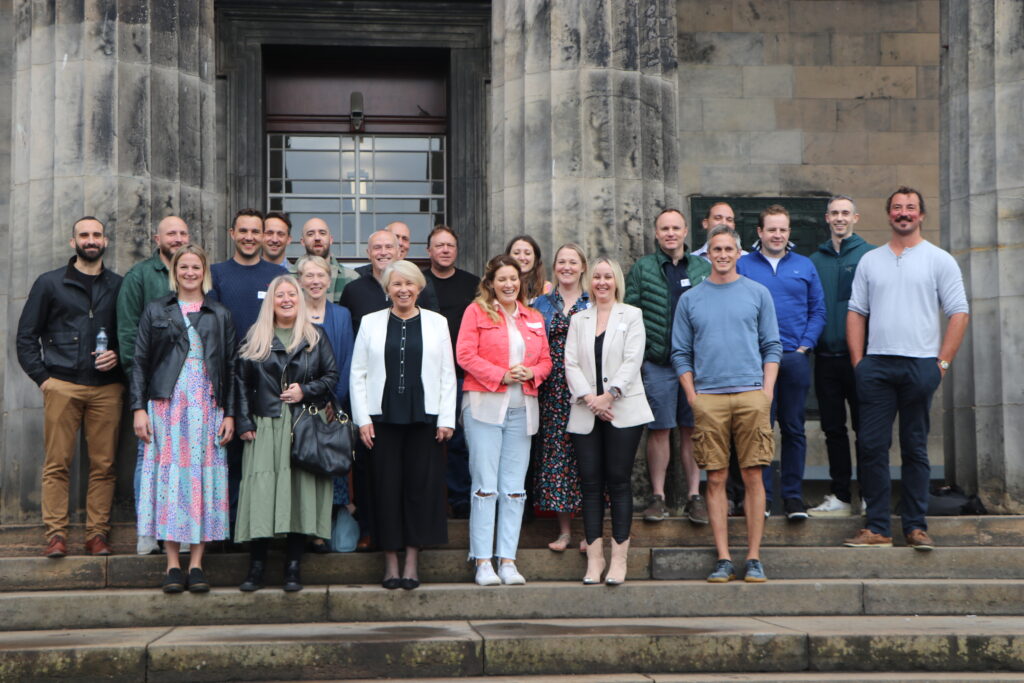 ALUMNI REUNION. Associates of the school standing on school steps by pillars looking cheerful.