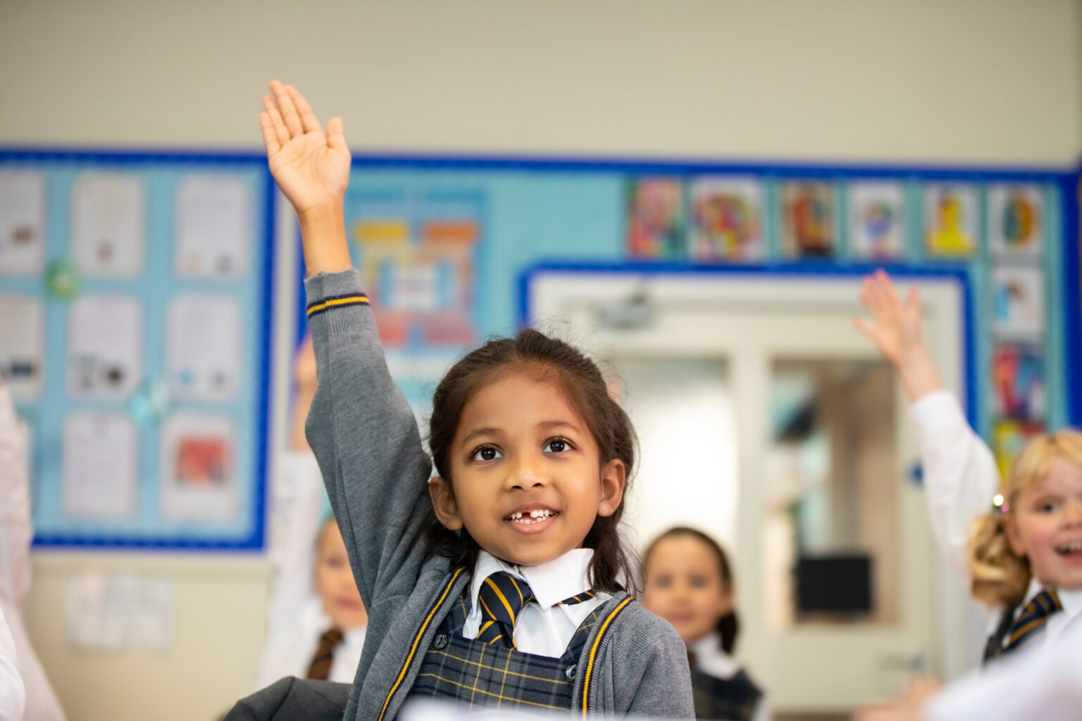 confidence hand up landscape. Pupils in class sat at desks with hands in the air eager to answer questions.