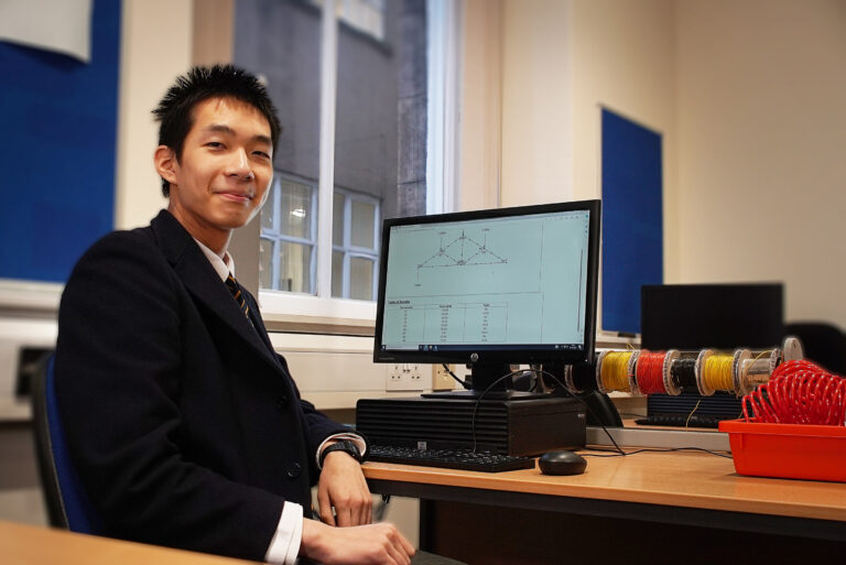 Pupil sits in front of computer in computing lab showing his calculations on the screen
