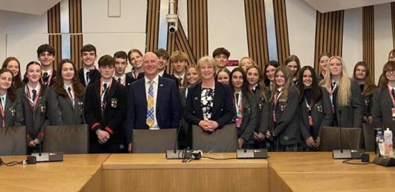 Pupils Observe Democracy At Work. Pupils and associates standing around a board room table.