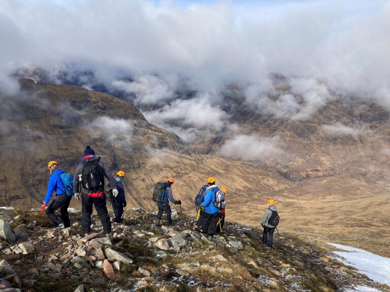 Winter Skills. Pupils and staff in rambling and caping gear, walking down a mountain towards a meadow.