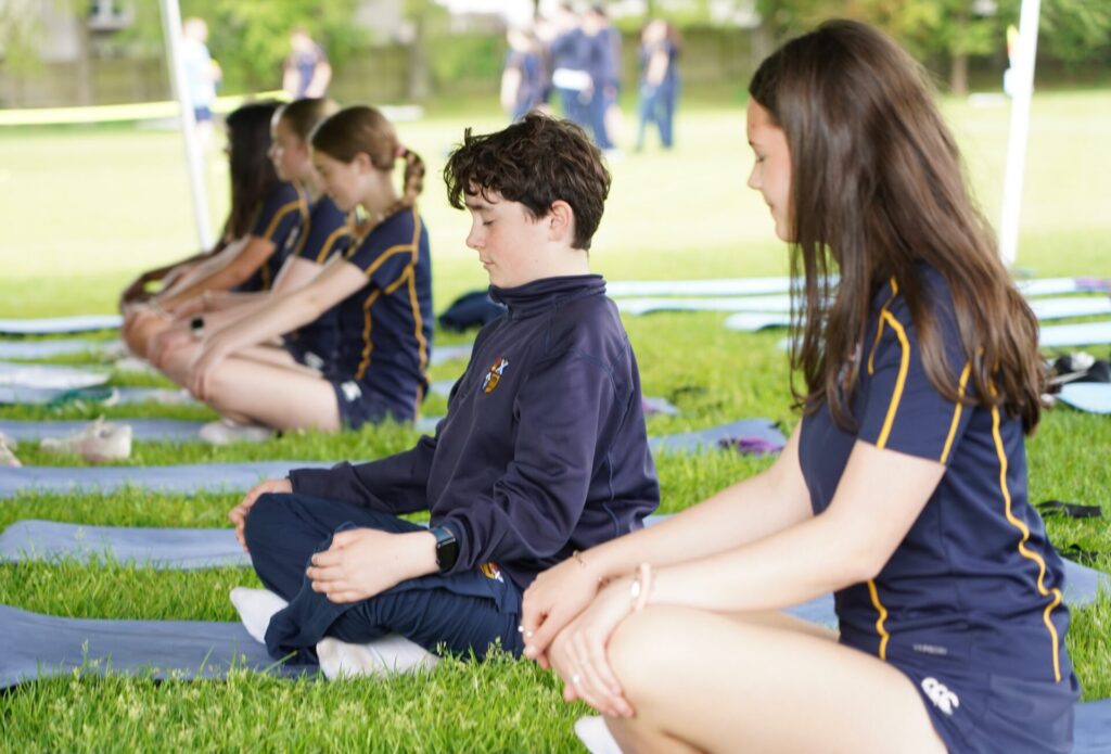 Pupils sit in yoga position and meditate with green grass all around